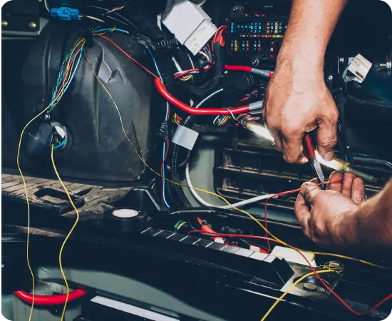 Close-up of hands using pliers to work with colorful electrical wires inside a car dashboard, showing automotive repair or wiring installation in progress.