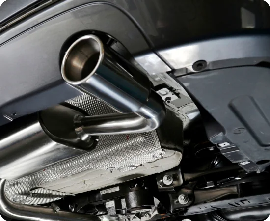 Close-up view of a car’s exhaust system and undercarriage, showing the shiny metal muffler and tailpipe beneath the vehicle.
