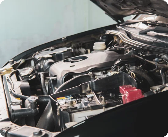 A close-up view of a car engine with the hood open, showing various engine components, battery, and cables.