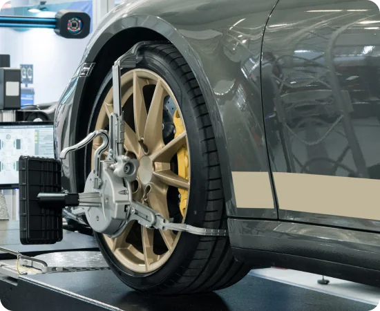 A close-up of a car wheel undergoing computerized alignment in a workshop, with sensors and equipment attached to the rim and tire.