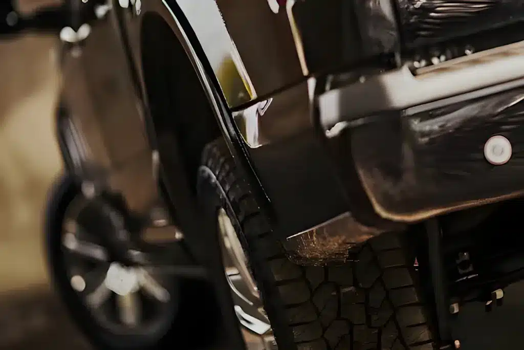 Close-up view of a black vehicles rear tire and bumper, with the focus on the textured tread of the tire and the shiny, reflective surface of the cars body.