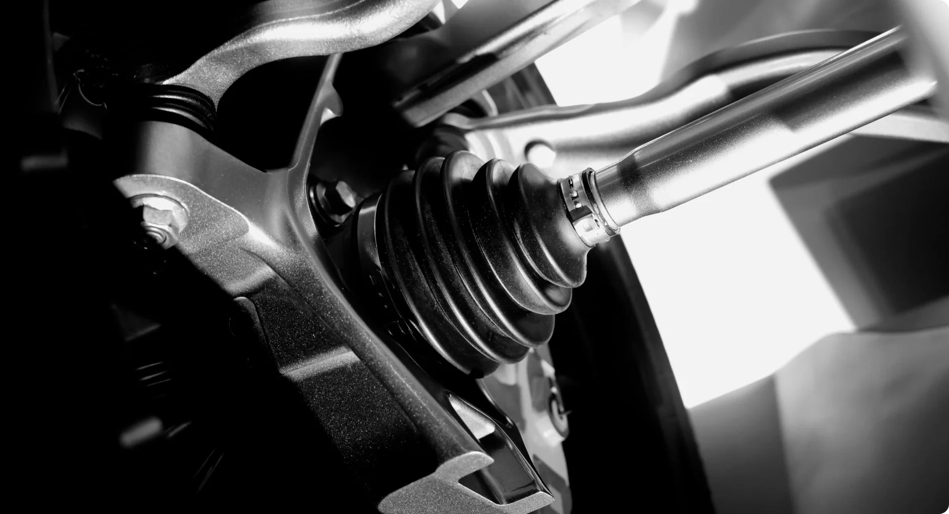 Close-up of a cars suspension and drive shaft assembly, highlighting the protective rubber boot and metallic components, shown in black and white with dramatic lighting.