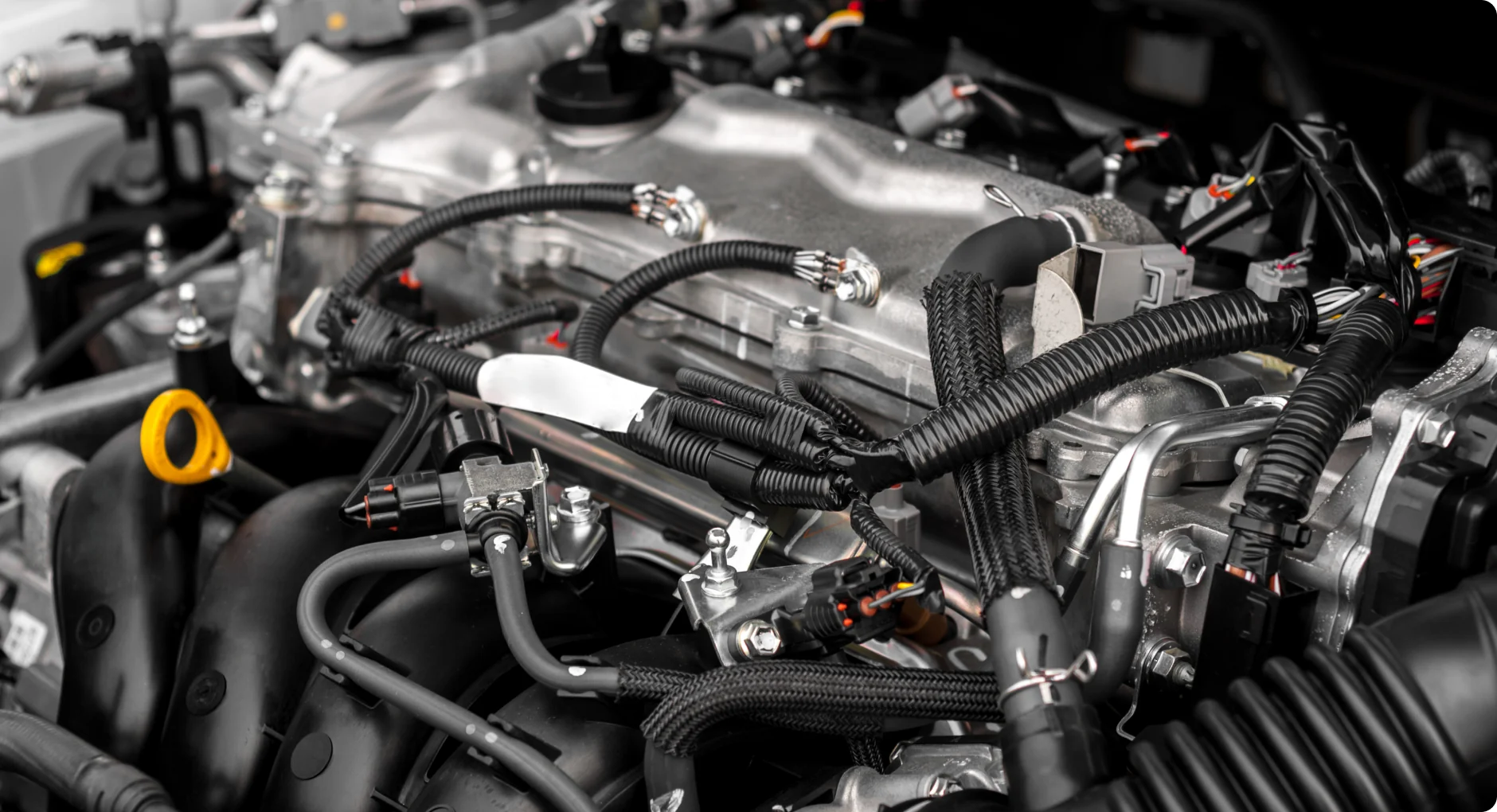 Close-up view of a modern car engine showing various metal components, black hoses, and electrical wiring, highlighting the complexity and detail of the engine compartment.